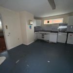 Empty kitchen with outdated appliances and peeling floor.