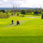 Two golfers walking on a sunny green course.