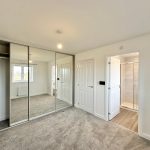 Modern bedroom with mirrored wardrobe and en-suite bathroom.