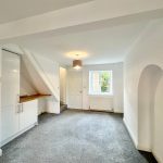 Spacious white living room with window and grey carpet.