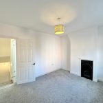 Bright, carpeted bedroom with fireplace and open door.