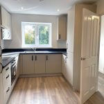 Modern grey kitchen with window and wooden floor.