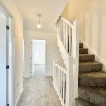 Modern hallway with carpeted stairs and bright room.