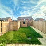 Fenced garden with grass and paving stones.