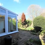 Garden with patio, shrubs, and conservatory.