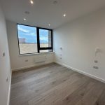 Empty modern room with wooden flooring and large window.