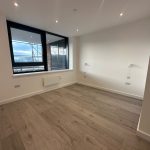 Empty room with wooden flooring and large window.