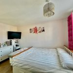 Bright bedroom with TV, dresser, and pink curtains.