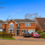 Modern detached brick house with driveway and two cars.