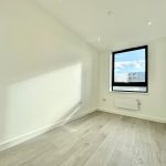 Bright empty room with wooden flooring and large window.