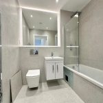 Modern grey-tiled bathroom with bathtub and mirror.