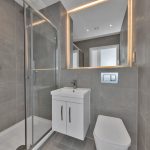 Modern grey bathroom with shower and large mirror.
