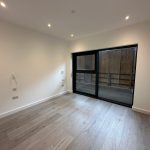 Empty room with large window and wood flooring.