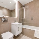 Modern beige-tiled bathroom with bathtub and vanity unit.