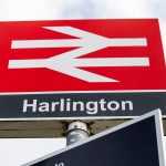 Harlington railway station sign with red background.
