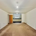 Spacious empty room with carpet and kitchen view.