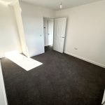 Empty room with carpet and white walls, light-filled.