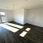 Bright empty room with wooden flooring and balcony view.