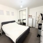 Modern white bedroom with mirrored wardrobe and artwork.