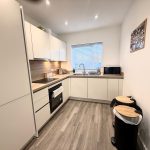Modern kitchen with white cabinets and wood flooring.