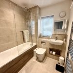 Modern bathroom with bathtub, sink, toilet, and towel rack.