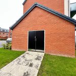 Red brick building with black doors and green lawn.