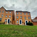 Three-storey brick houses with green lawn, overcast sky.