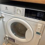 Electrolux washing machine in cupboard, door open.