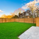Sunny backyard with grass, fence, and wooden shed.