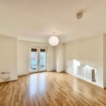 Bright, empty room with wooden flooring and balcony doors.