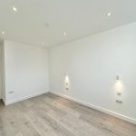 Minimalist empty room with wooden flooring and spotlights.