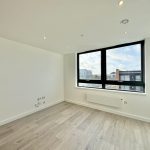 Bright empty room with large window and wooden floor.