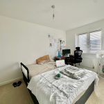 Modern bedroom with bed, desk, chair, and window.