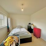 Bright, cluttered bedroom with bed, suitcase, fan.