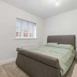 Modern bedroom with green bedding and clothes rack.