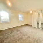 Bright bedroom with mirrored wardrobe and two windows.
