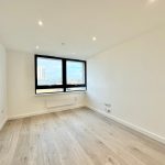 Bright empty room with large window and wooden floor.