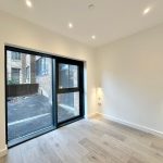 Empty room with large window and wooden floor.