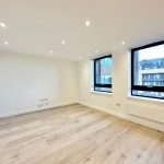 Spacious empty room with large windows and wooden floor.