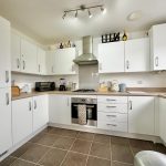 Modern white kitchen with appliances and overhead lights.