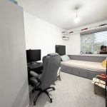 Modern bedroom with desk, computer, and window view.