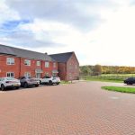 Red brick houses with parked cars and countryside view.