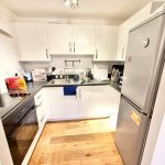 Modern kitchen with white cabinets and wooden flooring.
