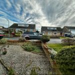 Residential street with parked cars and gardens.