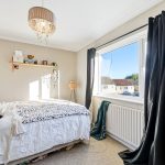 Cosy bedroom with bed, window view, and shelf.