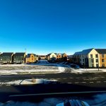 Snow-dusted street with modern houses under clear sky.