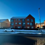 Snowy street with modern brick houses and car.