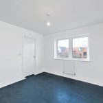 Empty white room with windows and unfinished floor.