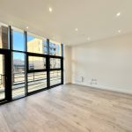 Empty modern flat with wooden flooring and large windows.