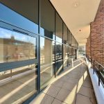 Sunlit walkway beside glass windows and brick wall.